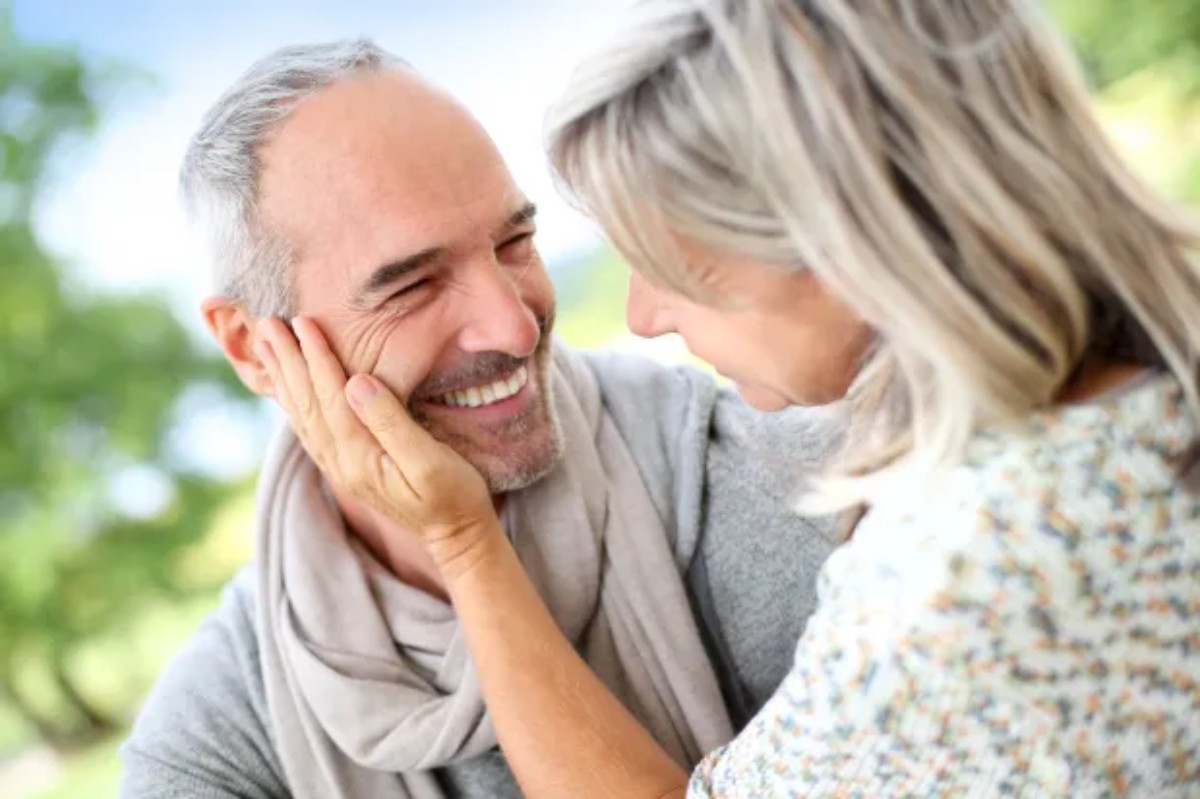 Un couple souriant se regarde tendrement en se touchant le visage, symbolisant l’amour profond et la complicité après 30 ans de mariage, pour illustrer les noces de perle.